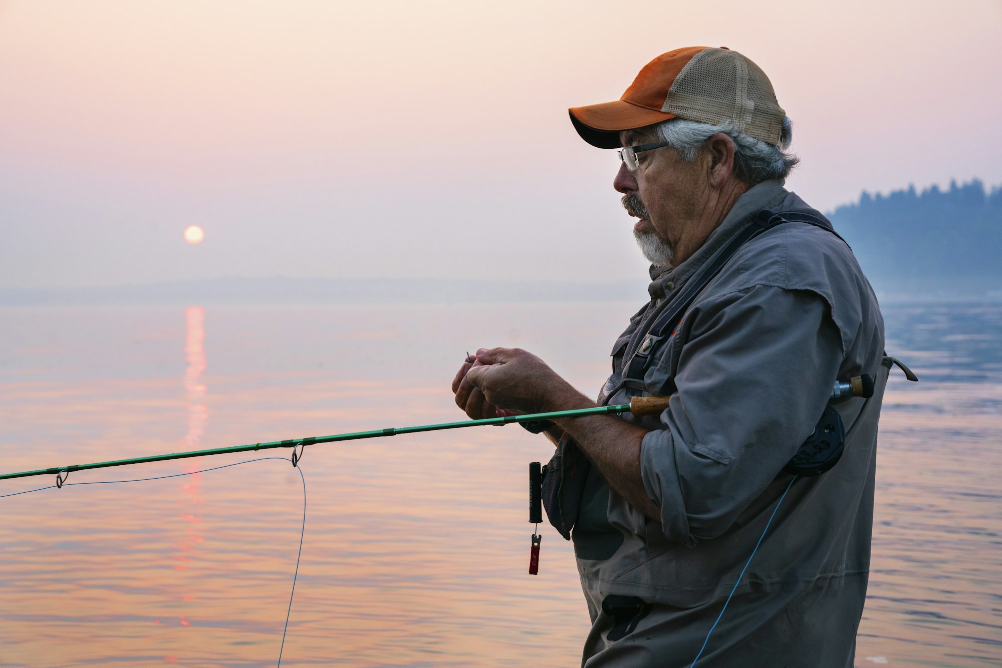 Caucasian man tying a fly on his fly fishing line while fishing for salmon and searun cutthroat