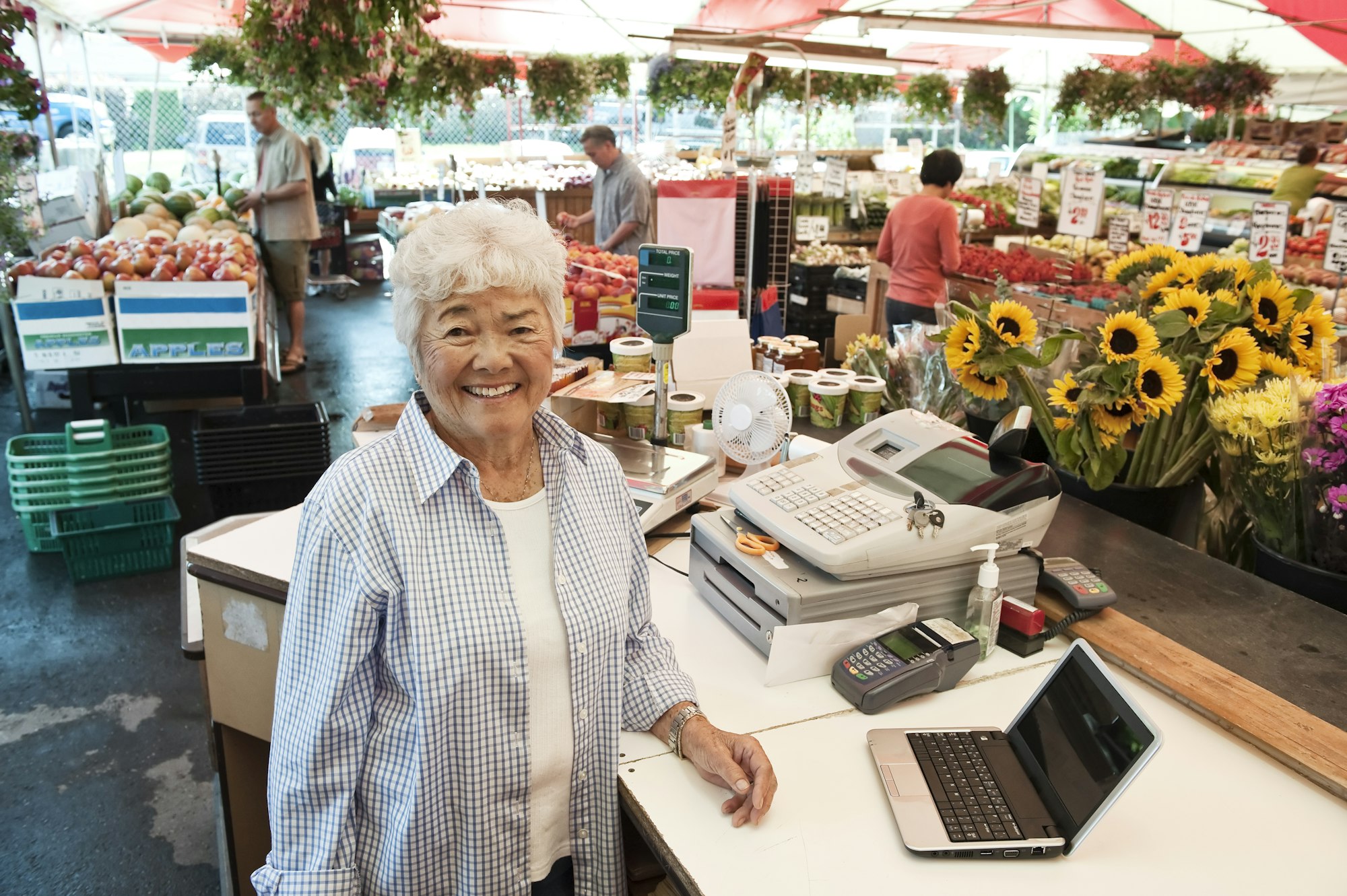 Senior woman standing at the checkout of a food and vegetable market, smiling at camera.